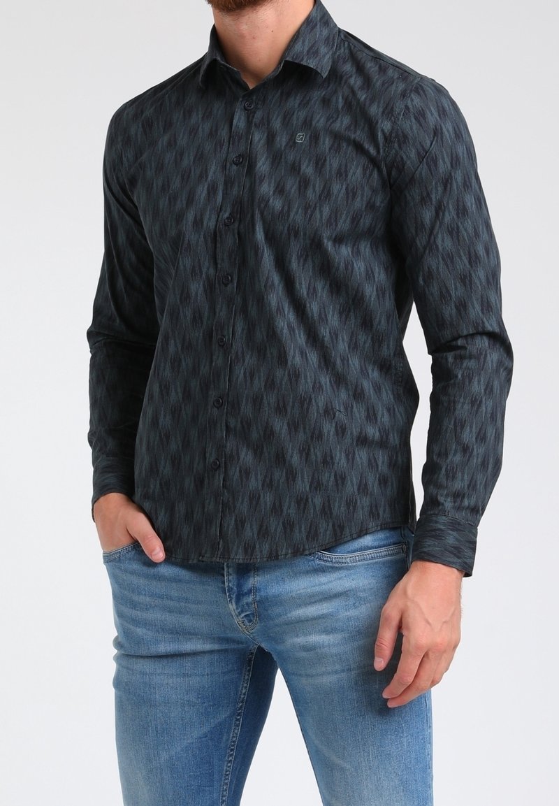 Chemise noire à motifs avec un design géométrique, manches longues et coupe décontractée, associée à un jean bleu clair.