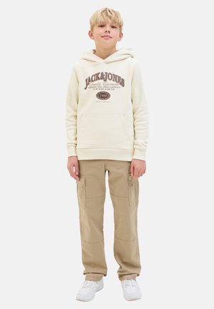 Sudadera crema con "JACK & JONES" impreso en marrón. Combinada con pantalones cargo beige que cuentan con múltiples bolsillos. Zapatillas blancas completan el atuendo.