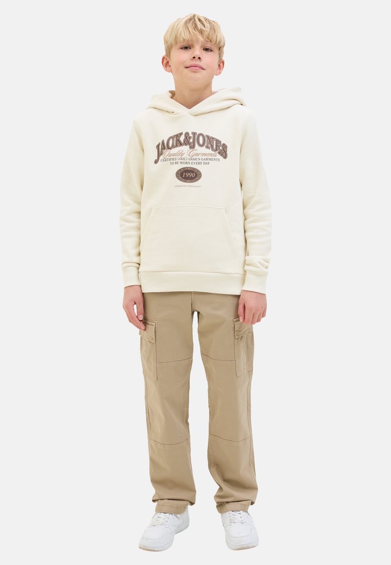 Un hoodie crème avec "JACK & JONES" imprimé en marron. Associé à un pantalon cargo beige avec plusieurs poches. Des baskets blanches complètent le look.