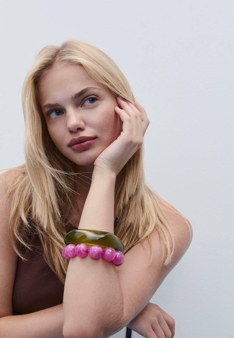 Bracciali in acrilico traslucido verde e rosa sul polso. Il bracciale verde è liscio, mentre quello rosa presenta perline rotonde.