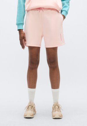Svetloružové teplákové šortky s elastickým pásom a sťahovacou šnúrkou. Majú bočné vrecká a malú ružovú nášivku na ľavom stehne.