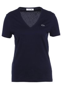 Granatowa koszulka z krótkim rękawem wykonana z bawełny, z dekoltem w serek i małym, haftowanym logo krokodyla po lewej stronie klatki piersiowej.