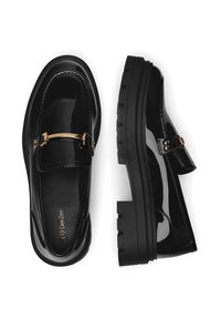 Mustmustaffid nahk ja viimistletud kummikud, millel on paks kummist põhi ja kuldne metallist detail, üks king pealtvaates, üks külgvaates, valgel taustal.