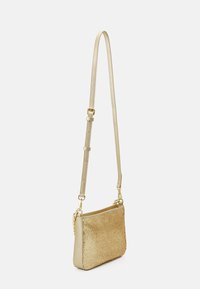 Gold crossbody bag with a textured surface. Features a long adjustable strap and a zippered top. Simple design with minimal hardware accents.