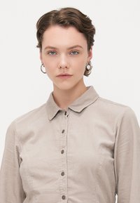 Camicia in corda beige con collo a punta, chiusura a bottoni e tessuto testurizzato. Sottile motivo a coste e forma aderente. Senza decorazioni esterne.