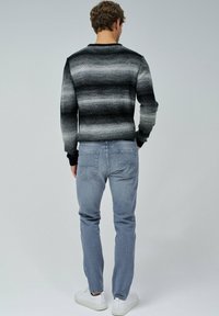 Jersey a rayas negro y gris con cuello redondo, combinado con jeans azul claro y zapatillas blancas. El jersey tiene un diseño ajustado.