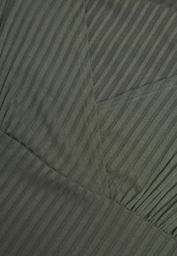 Tissu vert olive avec des rayures verticales, présentant un design texturé et plissé. Des coutures distinctives accentuent les coutures.