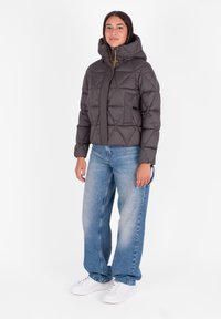 Donsjack in donkergrijs met een geborduurd patroon, een hoge kraag en een rits aan de voorkant. Gecombineerd met lichtblauwe denim jeans en witte sneakers.
