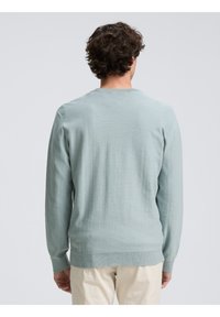Suéter azul claro hecho de material suave, con mangas largas y dobladillo acanalado. Presenta un clásico escote en cuello redondo y textura suave.