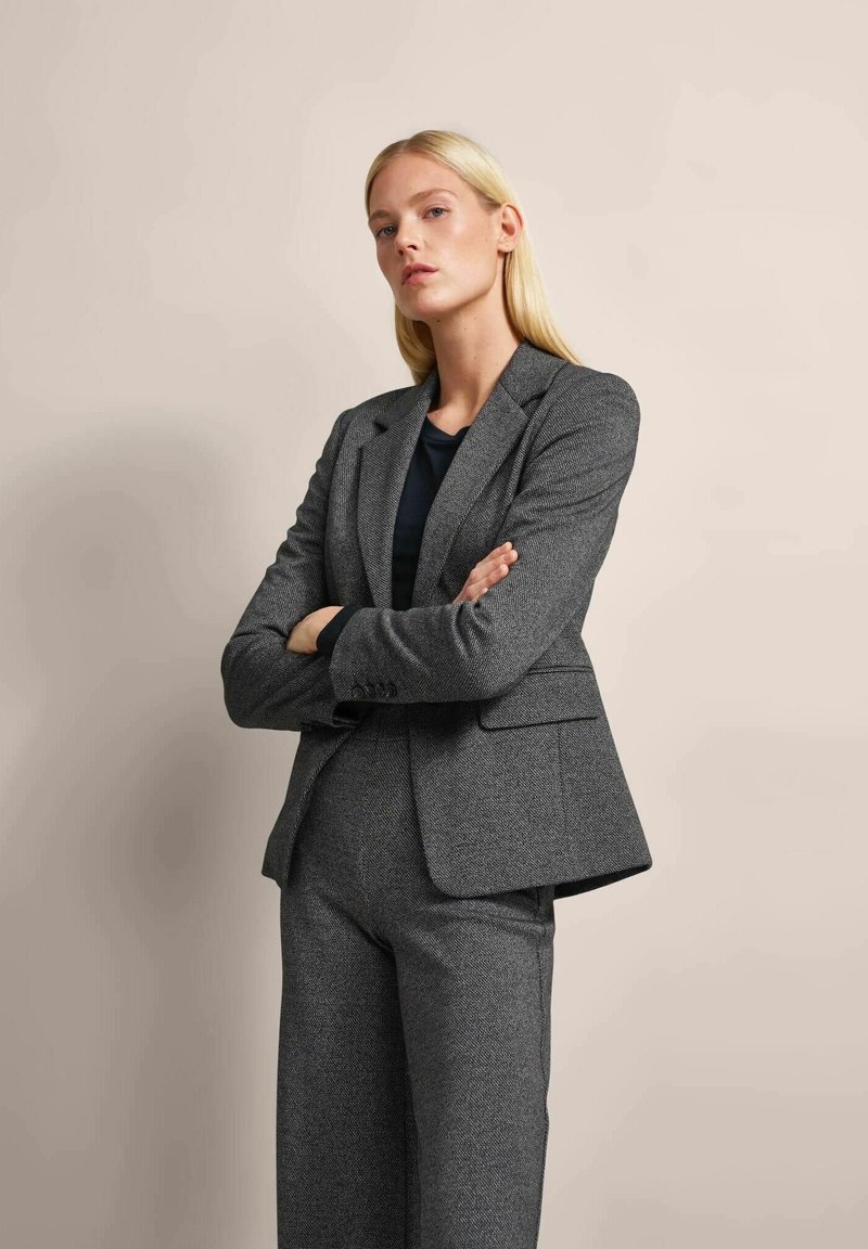 Gray textured blazer with notched lapels, two front pockets, and a tailored fit, paired with matching pants. Solid black top underneath.
