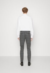 Grå rutiga byxor i vävt tyg, med slim fit och två bakfickor. Bärs med en vit skjorta med krage och svarta skor.