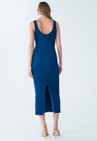 Vestito midi blu a coste con schiena ampia, spacco laterale e chiusura con zip. Presenta spalline sottili e una silhouette aderente.