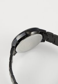 Montre en acier inoxydable noir avec une finition polie, boîtier rond et bracelet en métal. Présente une couronne texturée et un dos argenté lisse.