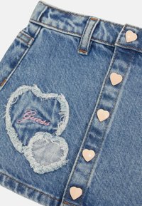 Világoskék farmer szoknya, szív alakú, rojtos hímzéssel és "Guess" felirattal. Az egyik oldalon rózsaszín szív alakú gombok találhatók.