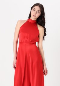 Robe rouge à col halter en tissu lisse, avec une taille cintrée et une jupe fluide. Silhouette élégante avec un design minimaliste.