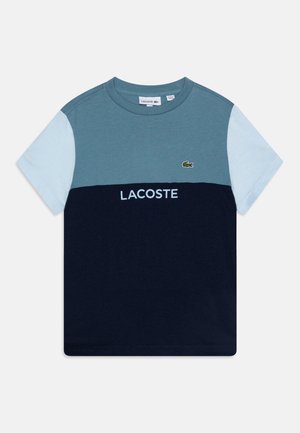 Krótki rękaw koszulki typu T-shirt z blokowym wzorem w kolorach niebiesko-zielonym i granatowym. Z logo Lacoste i okrągłym dekoltem. Wykonana z miękkiej bawełny.