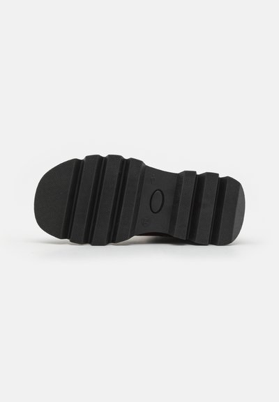 Suela de zapato de goma negra con una superficie texturizada que presenta ranuras horizontales y un emblema redondo en el centro.