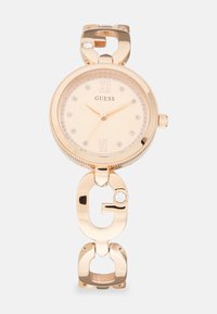 Goldfarbene Armbanduhr mit rundem Zifferblatt, funkelndem Rahmen und römischen Ziffern bei 12 und 6. Gliederarmband-Design mit einem G-förmigen Akzent.
