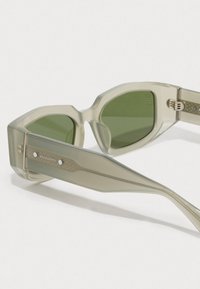 Óculos de sol retangulares translúcidos em bege com lentes verdes e hastes grossas, apresentando um detalhe em metal com a marca "AllSaints".