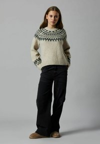 Suéter de punto en beige con un yugo gris oscuro estampado. Presenta puños y dobladillo acanalados. Combinado con jeans oscuros y calzado marrón.