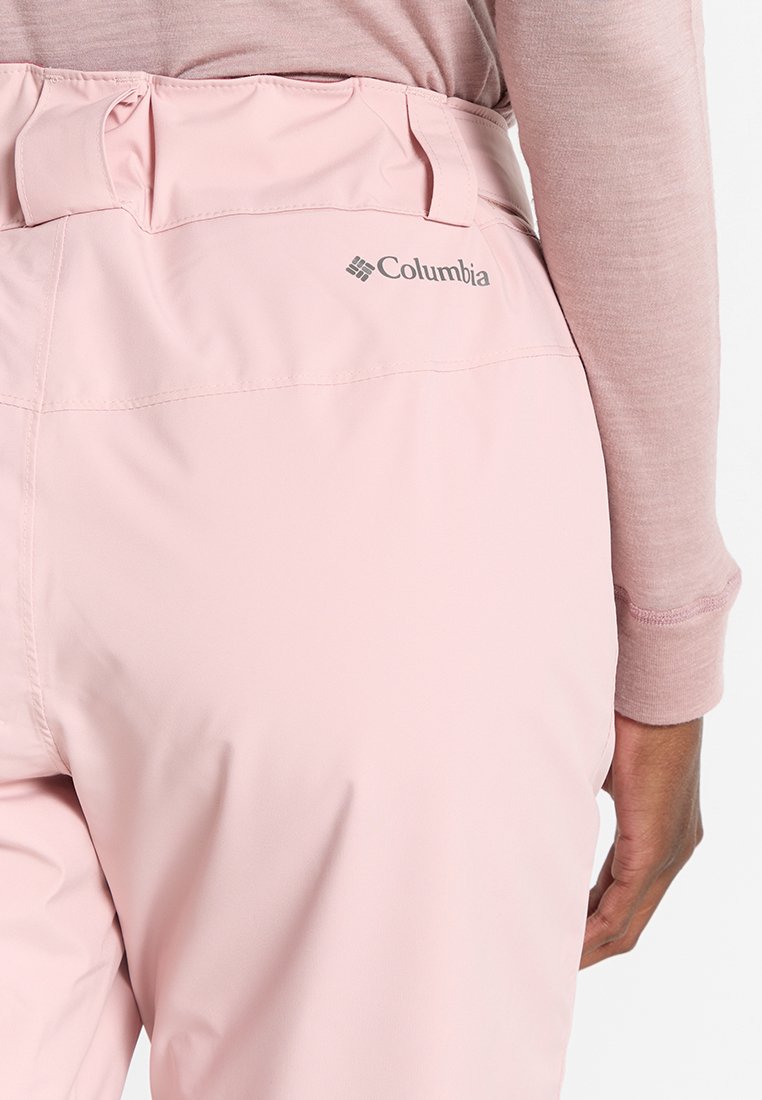 Jasnoróżowe spodnie Columbia z wysokim stanem i miękką teksturą. Posiadają elastyczny pas z fałdami oraz logo z tyłu.