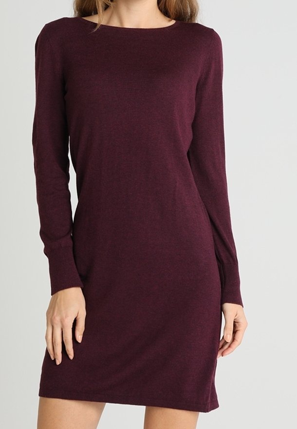 Femme portant une robe en maille ajustée, manches longues, longueur au genou, de couleur violet foncé, sur un fond clair uni.