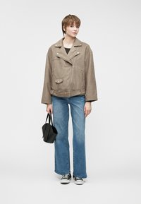 Brun faux suedet jakke med oversized passform, glidelås foran og belte i livet. Parret med utsvingte blå jeans og svart veske. Svart sneakers.