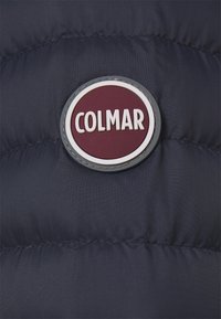Marinblå vadderad jacka med en rund vinröd logotyp och vit text "COLMAR", inramad av en texturerad kant.