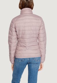Giubbotto imbottito rosa chiaro con design trapuntato, colletto alto e silhouette definita. Indossato sopra jeans blu, con una texture liscia e lucida.