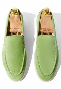 Mocasines de ante verde con un diseño elegante, paneles laterales elásticos y suelas de goma blancas. Incluye árboles para zapatos de madera y acentos dorados.