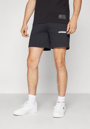 Zwarte sportshorts met een geprinte "HUMMEL" logo, gemaakt van zachte stof met een relaxte pasvorm, gecombineerd met witte sneakers en sokken.