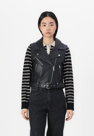 Zwart leren cropped motorvest met brede kraag, zilveren hardware, voorzakken met rits en verstelbare riem. Gekleed over een gestreepte lange mouwen shirt.