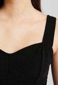 Schwarzes, geripptes Oberteil mit breiten Trägern, das einen herzförmigen Ausschnitt und einen strukturierten Stoff bietet. Das Design betont eine figurbetonte Silhouette.