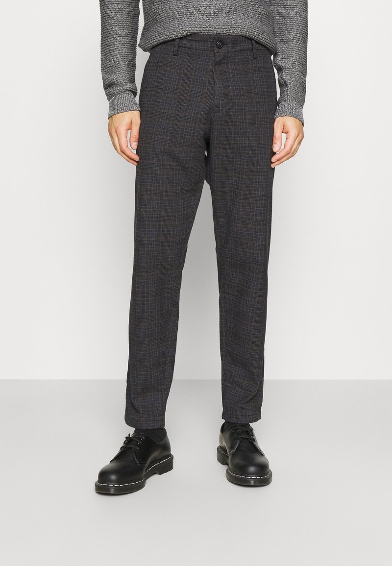 Tmavé kárované kalhoty s úzkým střihem, se vzorem v modré a hnědé barvě, s plochým předním dílem a bočními kapsami, doplněné černými botami.