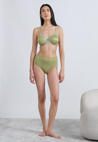 Zielony satynowy biustonosz z koronkowym wykończeniem oraz pasujące do niego, wysokie figi. Miękka tekstura. Regulowane ramiączka. Prosty, stonowany design.