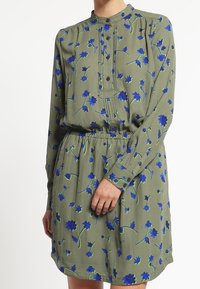 Zelené šaty s modrým květinovým vzorem, dlouhými rukávy, knoflíkovým zapínáním a elastickým páskem. Hladká látka s volným střihem.