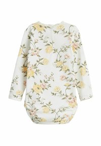Blommig långärmad plagg i vitt, med gula och rosa blommor, med en samlad hals och knappstängning bak. Mjuk tygtextur.