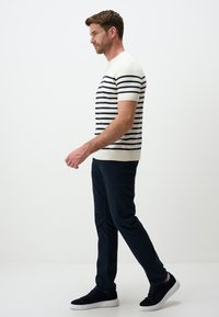 Męski sweter z krótkim rękawem w kolorze kremowym z granatowymi poziomymi paskami; zestawiony z ciemnymi spodniami i granatowymi trampkami. Prosty okrągły dekolt i dopasowany krój.