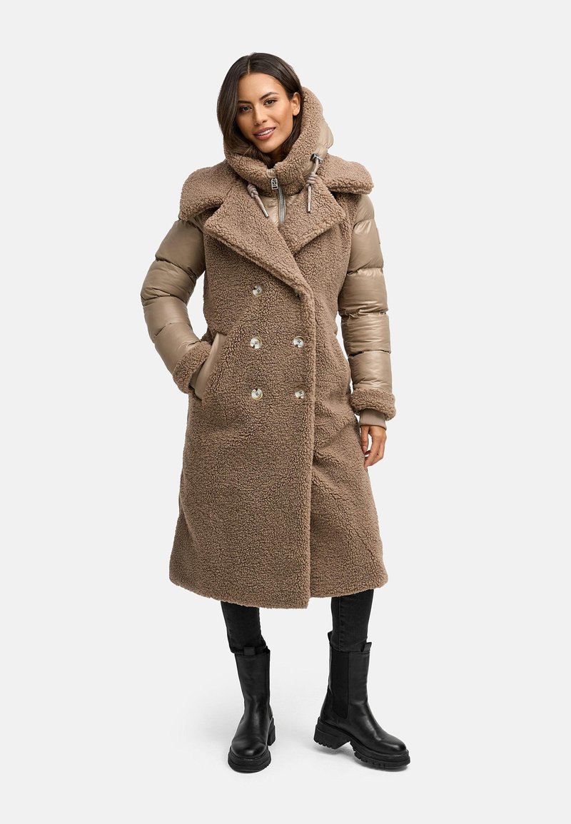 Cappotto lungo imbottito doppiopetto in marrone, con una trama esterna morbida, ampio colletto e tasche laterali, abbinato a stivaletti neri alla caviglia.