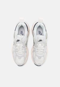 Nike-sneakers med ett ljusgrått meshnatt, vita overlay, marinblå accenter och en ljusrosa gummisula, med snörning och logodetaljer.