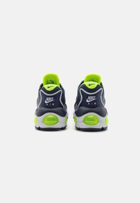 Nike Air-sneakers med en marinblå ovandel, limegröna accenter, vadderad sula och synliga luftkamrar i hälen. Texturerat tyg och logotypdetalj.