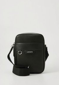 Bolso bandolera negro con acabado de cuero texturizado, que cuenta con cierre de cremallera, una correa ajustable y un detalle frontal con el logo en blanco.