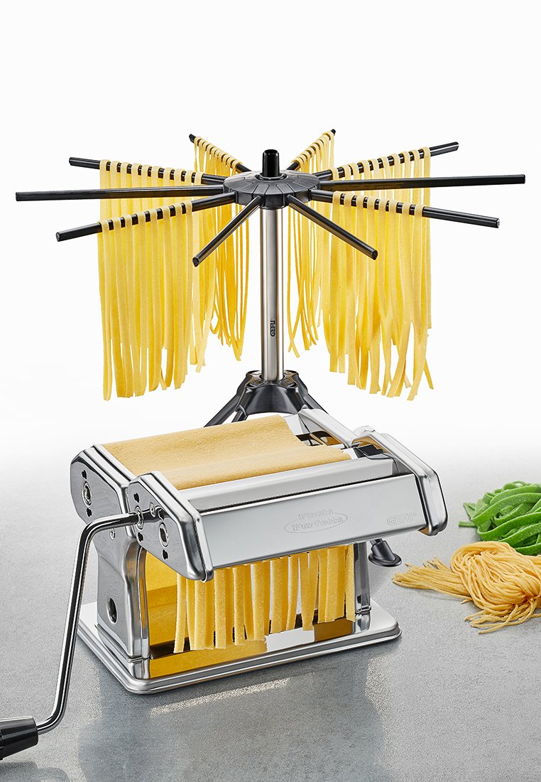 Nudelmacher mit Gehäuse aus Edelstahl, Handkurbel und abnehmbarem Trockenregal, das gelbe und grüne Nudeln hält.