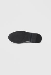 Semelle de chaussure noire avec une finition en caoutchouc lisse, présentant un talon légèrement surélevé et un motif texturé subtil pour une meilleure adhérence.