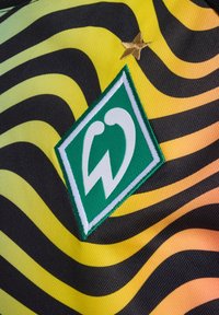 Grøn- og hvidt logo-patch på tekstureret stof med sorte og gule bølgede striber, der har en gul stjerne over logoet.