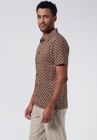 Korte mouwen shirt met een bruine basis, voorzien van een geometrisch patroon in oranje en crème. Met kraagontwerp, knoopsluiting en een relaxte pasvorm.