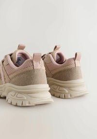 Baskets rose clair en mesh et suède. Talon arrondi, semelle épaisse avec des accents texturés. Deux poignées pour un enfilage facile.