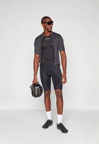 Čierny cyklistický outfit s priliehavým strihom, vrátane trička s krátkym rukávom a vypchávanych šortiek. Doplnky: čierna prilba a slnečné okuliare.