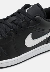 Black leather sneaker with white accents, featuring a prominent Swoosh logo, black laces, and a textured rubber sole.