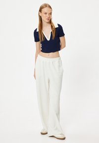 Top corto blu navy con colletto bianco, abbinato a pantaloni della tuta bianchi larghi. L'outfit è realizzato in tessuto morbido e traspirante, che offre comfort.